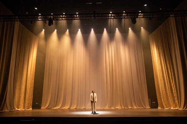 Stage performance moment Man standing on stage under spotlight, surrounded by golden curtains